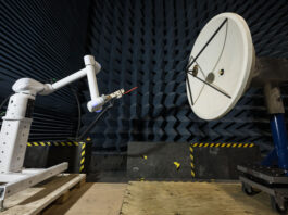 NASA Enhances Lunar Communication with Electric Field Tests: Earth to Gateway In a testing facility, a robotic arm manipulates a probe to test the electric field of a large, white, circular dish antenna. This antenna is situated within an anechoic chamber, which is lined with dark blue, wedge-shaped foam.