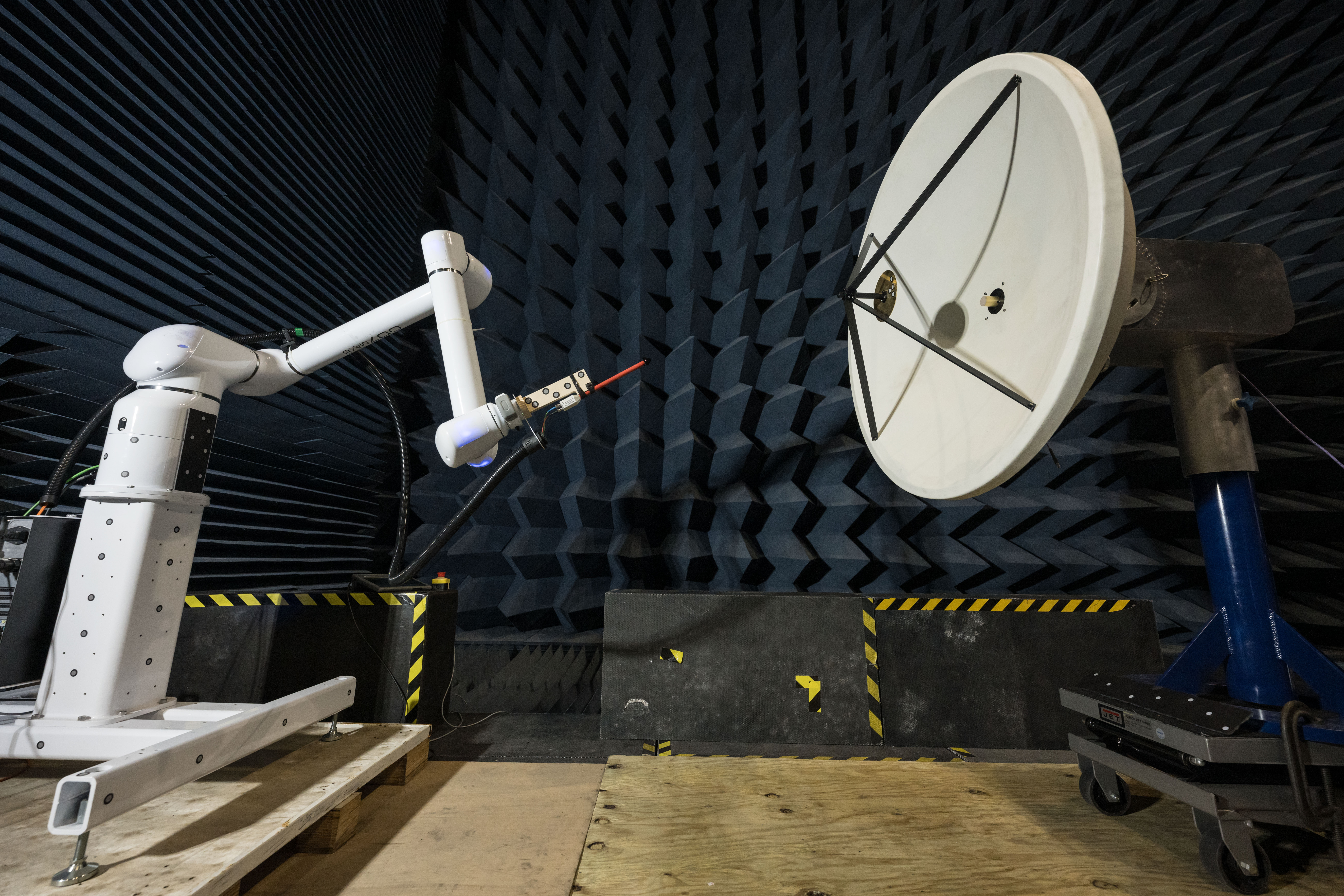 jsc2024e024307 1.jpg In a testing facility, a robotic arm manipulates a probe to test the electric field of a large, white, circular dish antenna. This antenna is situated within an anechoic chamber, which is lined with dark blue, wedge-shaped foam.