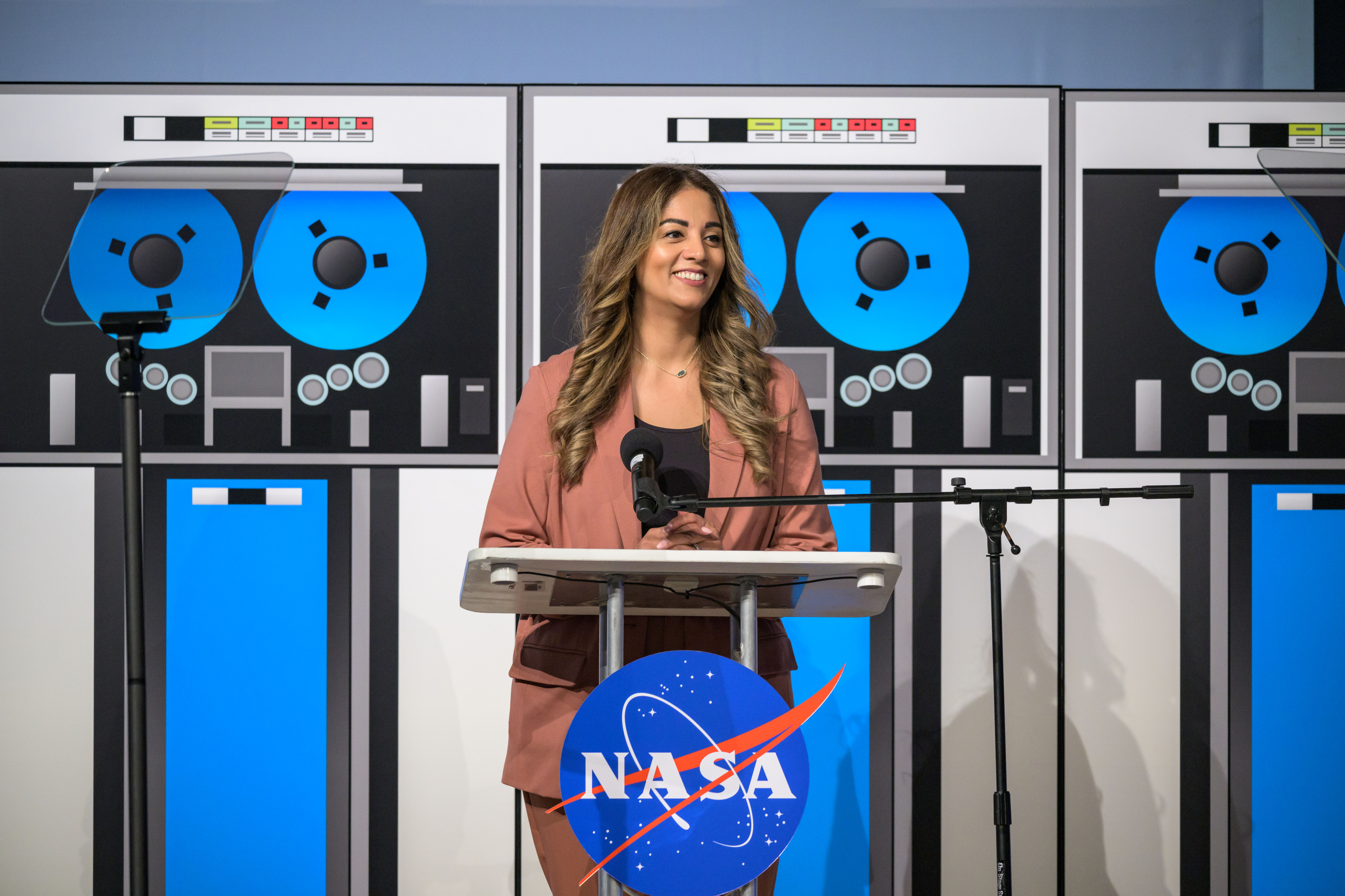 jsc2024e049794.jpg A woman dressed in a light brown suit smiles and stands at a podium during an event.