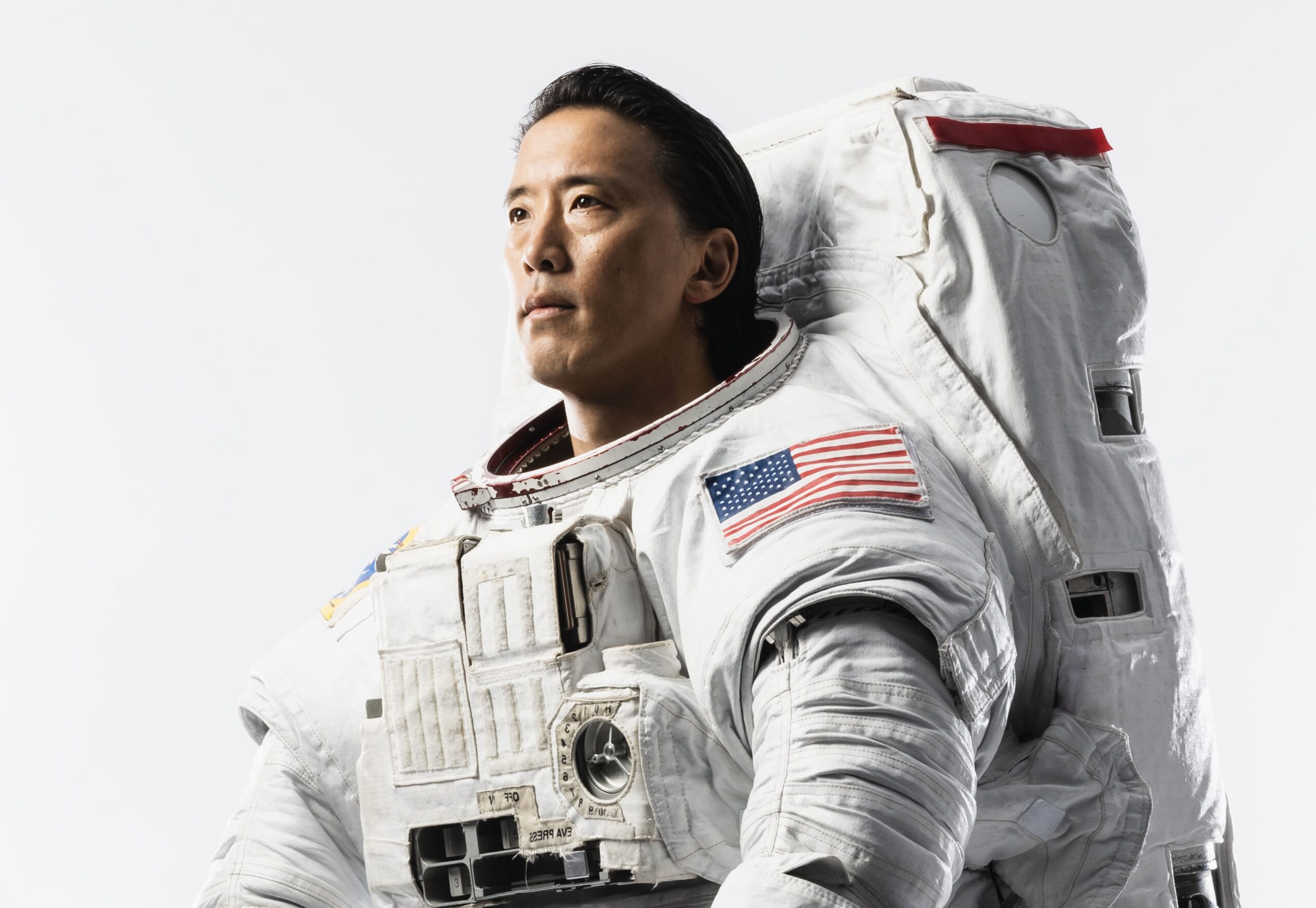 jsc2024e052673 altorig.jpg NASA astronaut Jonny Kim looks off-camera, dressed in a white space suit with an American flag on the sleeve.