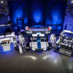 NASA Evaluates Commercial Rovers for Upcoming Lunar Missions Three lunar terrain vehicles side by side inside of a large chamber with dramatic lighting. Astrolab
