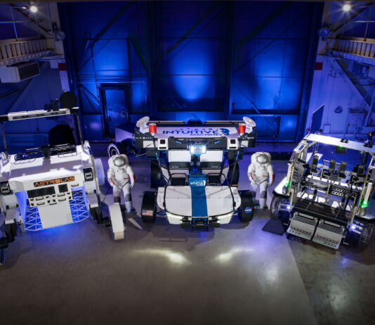 NASA Evaluates Commercial Rovers for Upcoming Lunar Missions Three lunar terrain vehicles side by side inside of a large chamber with dramatic lighting. Astrolab