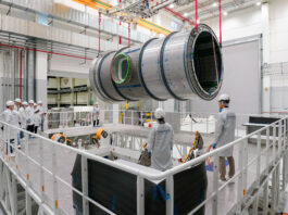 Lunar Module Heads to U.S. for NASA’s Artemis IV Mission A large cylindrical module is suspended by red straps as it is lowered onto a stand in a cleanroom at Thales Alenia Space in Turin, Italy. Engineers and technicians in white lab coats and helmets observe and guide the process from an elevated platform. The cleanroom features metal walkways and bright overhead lighting.