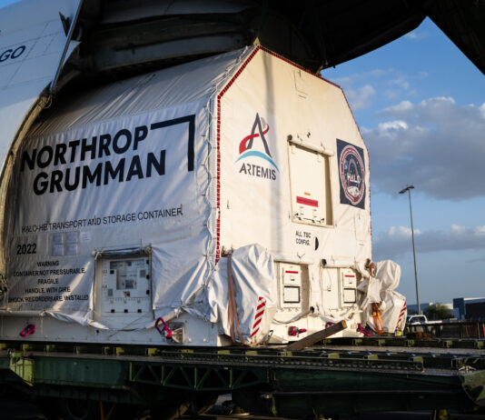 NASA Celebrates Arrival of HALO Module for Lunar Gateway A large cargo aircraft with its nose lifted open reveals a wrapped container being offloaded. The container is marked with the logo for NASA