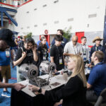 NASA Integrates Space Exploration into FIRST Robotics 2025 Two people sit at a booth with space exploration materials. They are engaging with the public at an event.