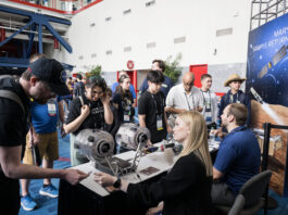 NASA Integrates Space Exploration into FIRST Robotics 2025 Two people sit at a booth with space exploration materials. They are engaging with the public at an event.