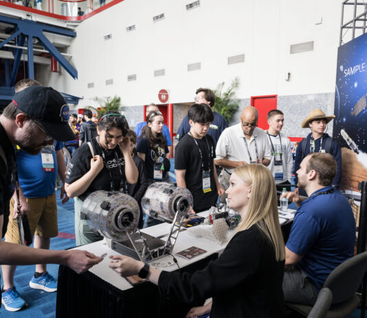 NASA Integrates Space Exploration into FIRST Robotics 2025 Two people sit at a booth with space exploration materials. They are engaging with the public at an event.