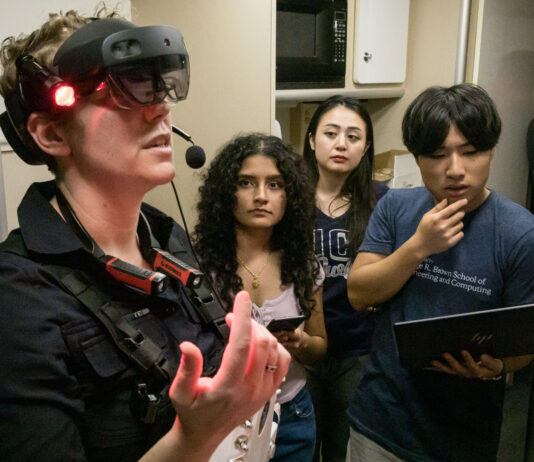 Student Teams Conclude NASA Space Suit Challenge Successfully A woman wears a virtual reality headset with three people observing behind her.
