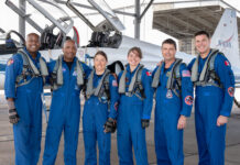 Artemis II Crew Receives NASA’s Farewell Before Mission Departure From left to right, NASA astronauts Andre Douglas, Victor Glover, and Christina Koch, CSA (Canadian Space Agency) astronauts Jenni Gibbons, NASA astronaut Reid Wiseman, and CSA astronaut Jeremy Hansen pose in front of an airplane. They are all wearing blue jumpsuits with patches and gray harnesses.