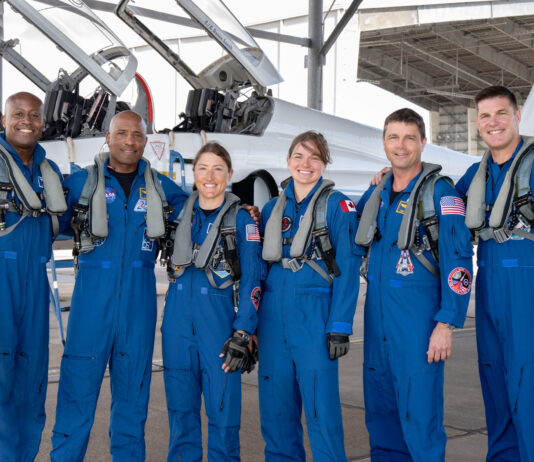 Artemis II Crew Receives NASA’s Farewell Before Mission Departure From left to right, NASA astronauts Andre Douglas, Victor Glover, and Christina Koch, CSA (Canadian Space Agency) astronauts Jenni Gibbons, NASA astronaut Reid Wiseman, and CSA astronaut Jeremy Hansen pose in front of an airplane. They are all wearing blue jumpsuits with patches and gray harnesses.