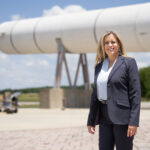 Meet Julia Khodabandeh: NASA’s Artemis Program Star A blonde woman stands in front of a rocket booster in a grey jacket.