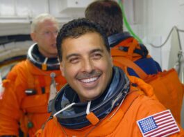 José Hernández Joins NASA’s Discovery Mission Astronaut José Hernández, a Hispanic man, smiles broadly at the camera while waiting to board space shuttle Discovery. He wears an orange escape suit that has an American flag patch on the left shoulder. Behind him are mission specialists Patrick Forrester (left) and Christer Fuglesang (back to camera).
