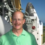 Michael Ciancone Leaves Enduring Impact on Human Spaceflight at NASA A man wearing a neon green polo smiles outside on a sunny day in front of a space shuttle.