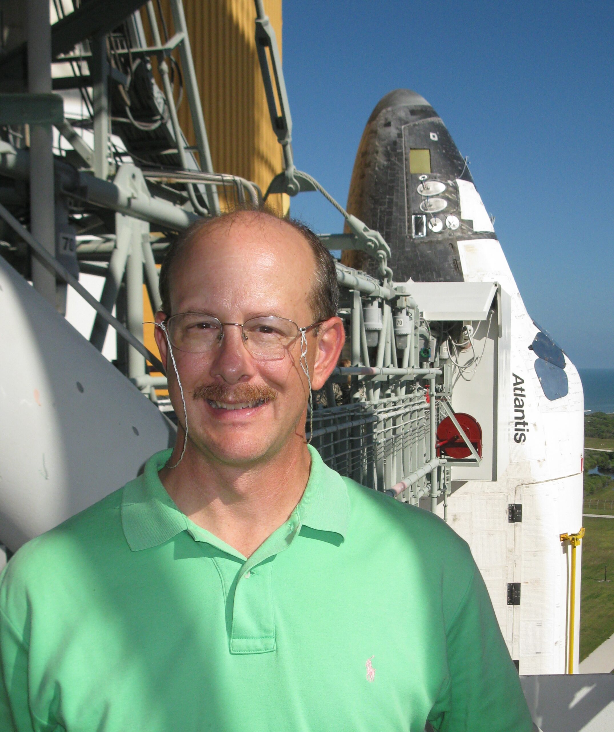 ksc 2009 cropped.jpg A man wearing a neon green polo smiles outside on a sunny day in front of a space shuttle.