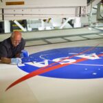 NASA Celebrates 65 Years of Iconic Logo, Media Invited Image of a man on the ground painting blue on the NASA meatball logo.