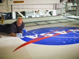 NASA Celebrates 65 Years of Iconic Logo, Media Invited Image of a man on the ground painting blue on the NASA meatball logo.