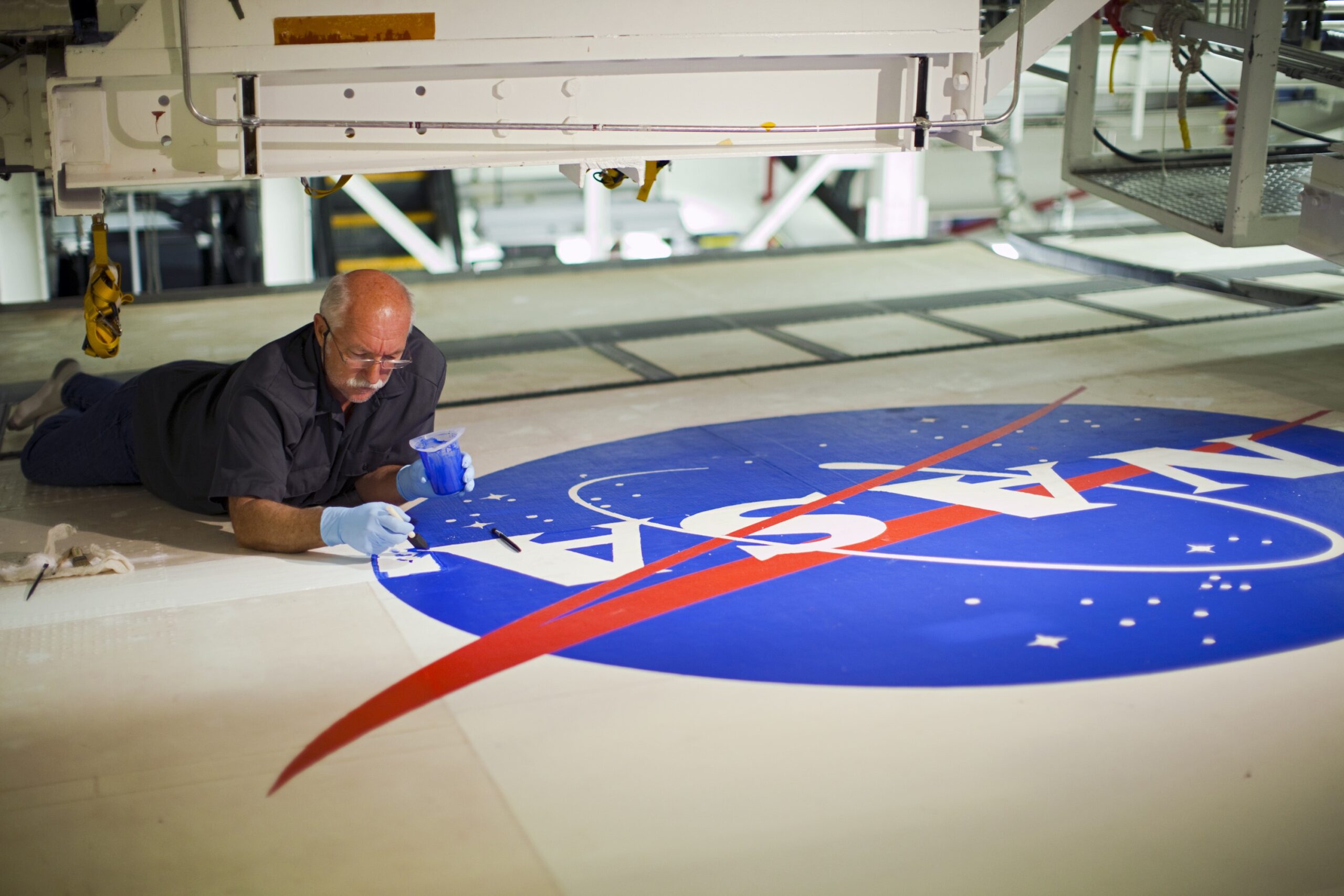 ksc 2012 2602orig.jpg Image of a man on the ground painting blue on the NASA meatball logo.