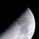 NASA’s Ambitious Plans for Lunar Exploration The Moon is lit so only half of it, diagonally, is visible. Along that line, craters of different sizes are visible. As you look toward the right, you can see light and dark gray areas on the Moon