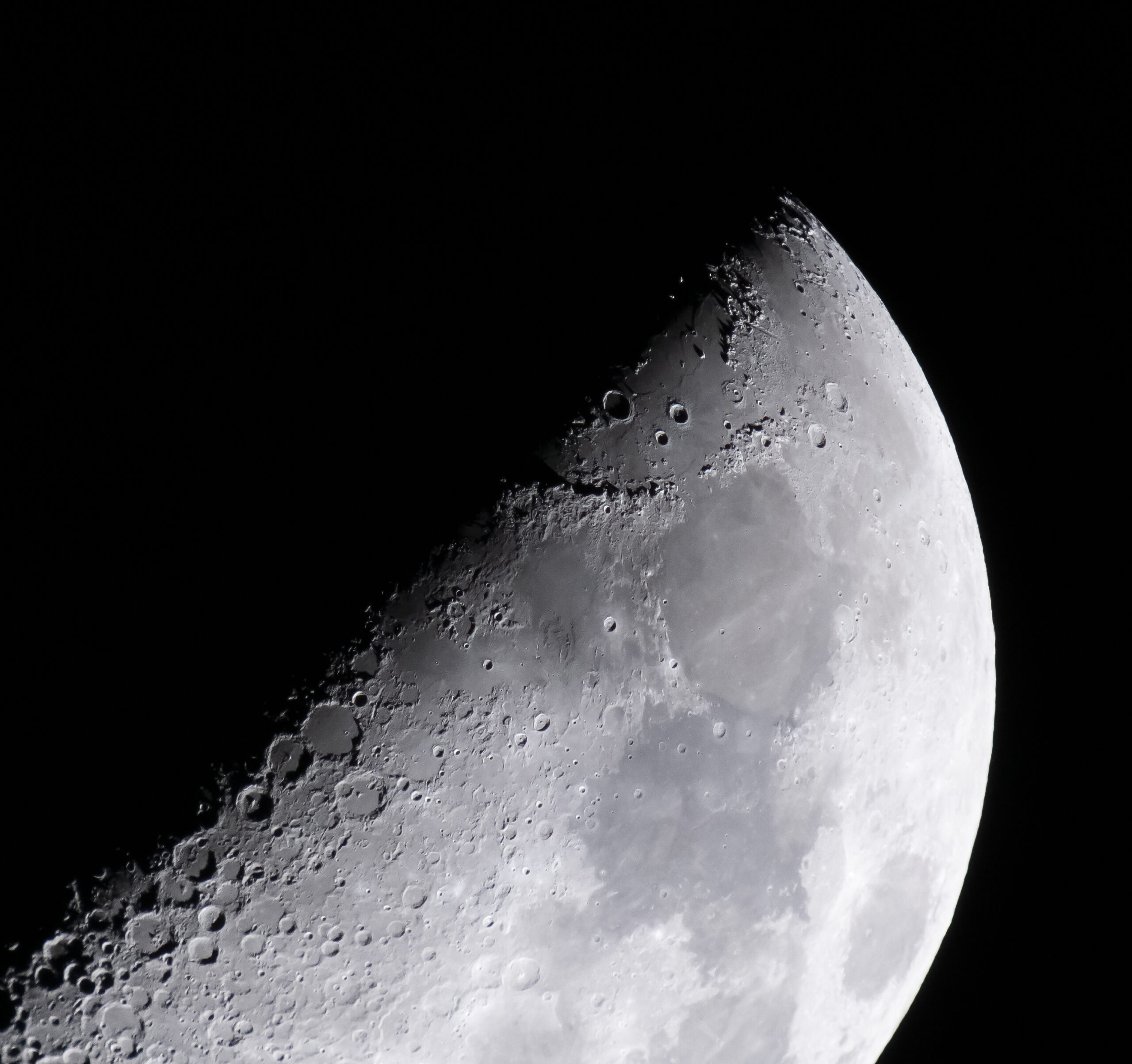 The Moon is lit so only half of it, diagonally, is visible. Along that line, craters of different sizes are visible. As you look toward the right, you can see light and dark gray areas on the Moon