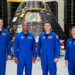 NASA Launches Twitch Stream: Create Artemis II Moon Mascot Four Artemis II astronauts in their blue flight suits stand smiling in front of a cone-shaped black-and-silver Orion spacecraft.