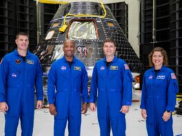 NASA Launches Twitch Stream: Create Artemis II Moon Mascot Four Artemis II astronauts in their blue flight suits stand smiling in front of a cone-shaped black-and-silver Orion spacecraft.