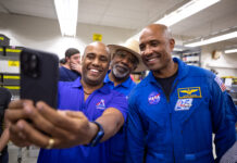 Astronaut Victor Glover Hosts Selfie Session with NASA Fans Three African American men - two Kennedy Space Center employees wearing blue polo shirts with an Artemis logo (left, middle back) and NASA astronaut Victor Glover (right) - pose for a photo taken with a cell phone.
