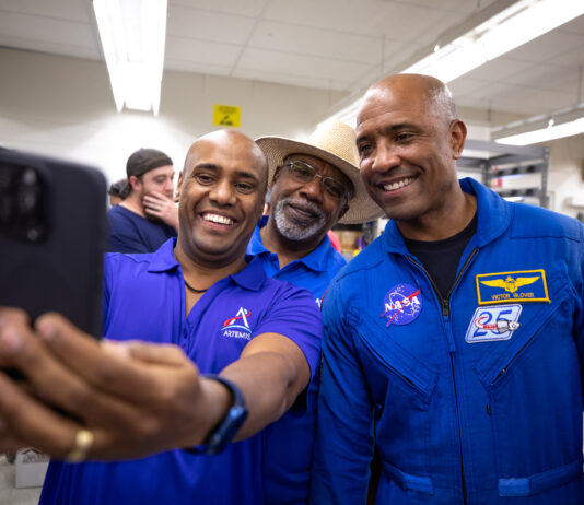 Astronaut Victor Glover Hosts Selfie Session with NASA Fans Three African American men - two Kennedy Space Center employees wearing blue polo shirts with an Artemis logo (left, middle back) and NASA astronaut Victor Glover (right) - pose for a photo taken with a cell phone.