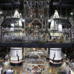 NASA Finishes Stacking Rocket Boosters for Artemis II Mission Two massive white rocket boosters stand inside the Vehicle Assembly Building. There are balconies and stairs around the boosters, reaching all the way up to the recently integrated nose cones.