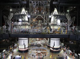 NASA Finishes Stacking Rocket Boosters for Artemis II Mission Two massive white rocket boosters stand inside the Vehicle Assembly Building. There are balconies and stairs around the boosters, reaching all the way up to the recently integrated nose cones.