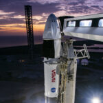 Crew-10 Awaits Launch as Dawn Breaks at NASA Pad The upper portion of a rocket with a spacecraft on top are visible in this picture. Both NASA logos are visible - the