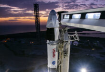 Crew-10 Awaits Launch as Dawn Breaks at NASA Pad The upper portion of a rocket with a spacecraft on top are visible in this picture. Both NASA logos are visible - the
