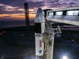 Crew-10 Awaits Launch as Dawn Breaks at NASA Pad The upper portion of a rocket with a spacecraft on top are visible in this picture. Both NASA logos are visible - the