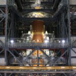 NASA Completes Artemis II Orion Spacecraft Stacking The orange core stage of the Artemis II rocket with white boosters on each side fully stacked inside the Vehicle Assembly Building at NASA
