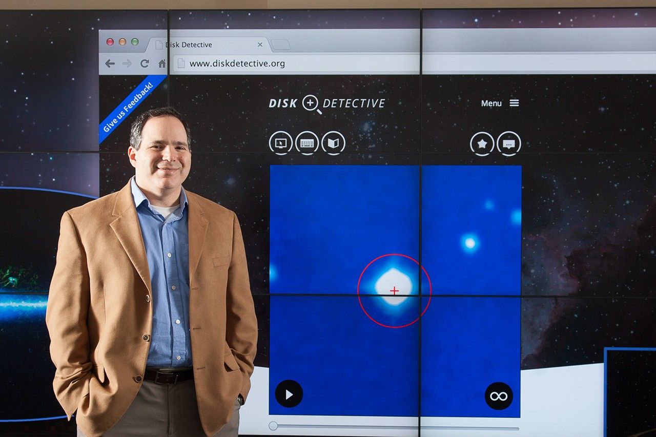 Photo of a man standing next to a large projected image of the Disk Detective website
