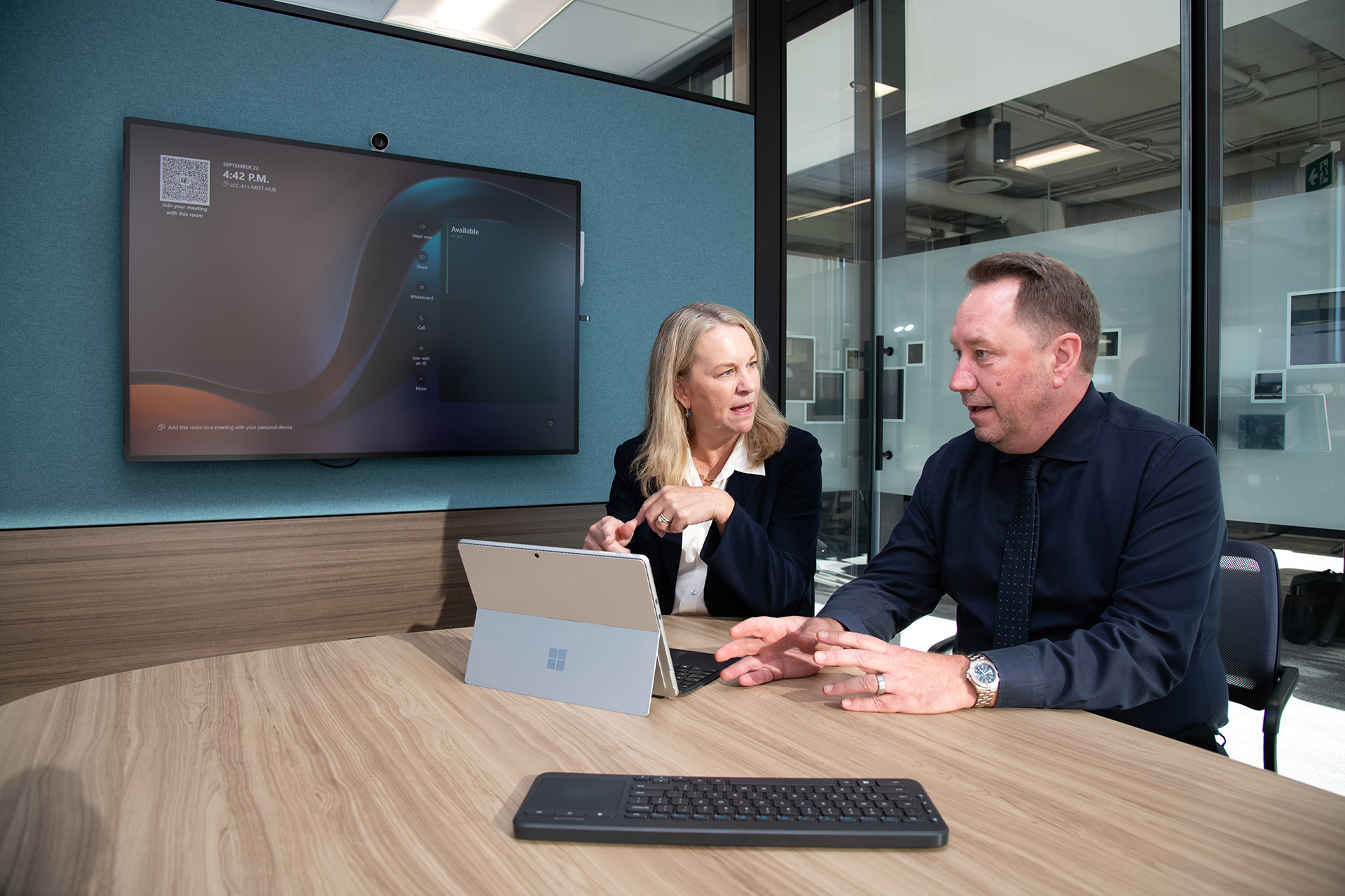 launi skinner darrel jaggers.jpg A man and a woman sit at a table in a conference room working on a Surface tablet