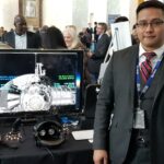 Lee Bingham Heads Lunar Simulation Support for NASA Artemis Mission NASA employee Lee Bingham, wearing a dark suit with a vest and red tie, stands next to a computer monitor with a Gateway simulation displayed on the screen.