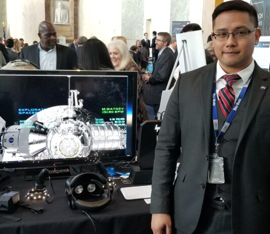 Lee Bingham Heads Lunar Simulation Support for NASA Artemis Mission NASA employee Lee Bingham, wearing a dark suit with a vest and red tie, stands next to a computer monitor with a Gateway simulation displayed on the screen.