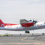 NASA Reveals New Colors on Research Plane for Hybrid Electric Tests A four-engine turboprop aircraft in a red and white livery takes off from a runway on its way to be modified into a hybrid electric aircraft. Other airplanes can be seen in the distance.