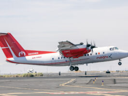 NASA Reveals New Colors on Research Plane for Hybrid Electric Tests A four-engine turboprop aircraft in a red and white livery takes off from a runway on its way to be modified into a hybrid electric aircraft. Other airplanes can be seen in the distance.