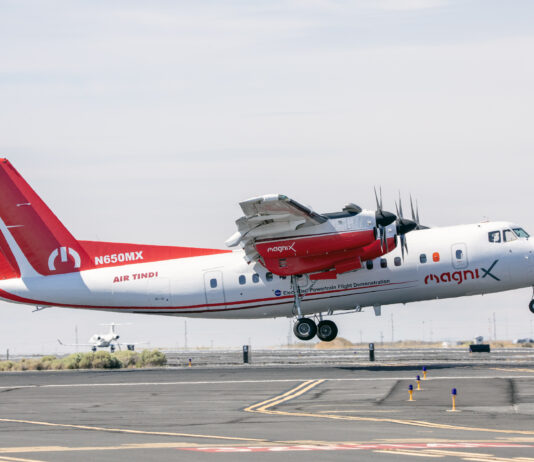 NASA Reveals New Colors on Research Plane for Hybrid Electric Tests A four-engine turboprop aircraft in a red and white livery takes off from a runway on its way to be modified into a hybrid electric aircraft. Other airplanes can be seen in the distance.