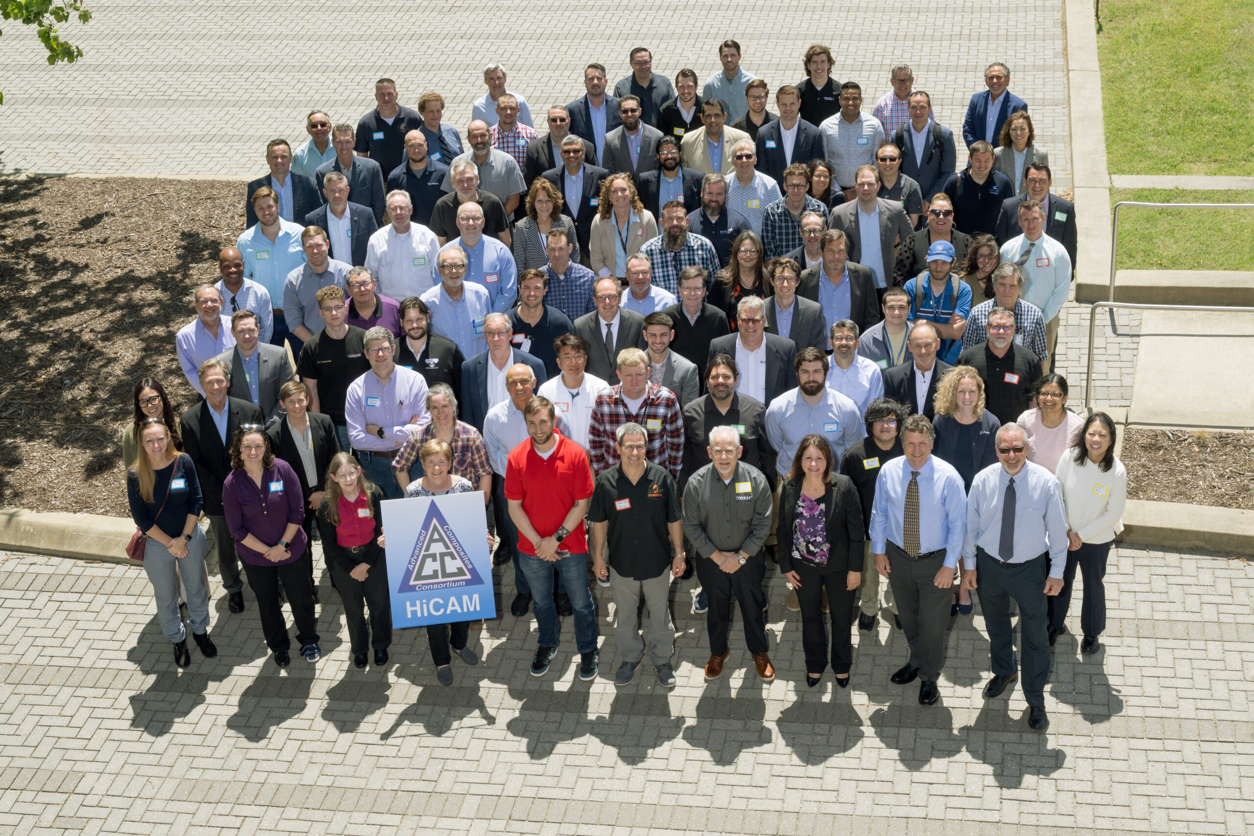A large group of people who work on composite aircraft pose outside in a parking lot.