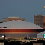 NASA Captures Stunning Moon Above Superdome The full moon (top right) rises over buildings in New Orleans, Louisiana, including the Superdome. The Superdome has a white rounded top. Billboards and ads can be seen around and on some of the buildings.