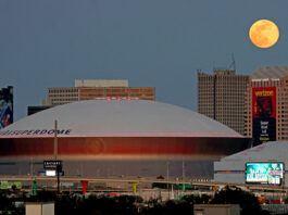 NASA Captures Stunning Moon Above Superdome The full moon (top right) rises over buildings in New Orleans, Louisiana, including the Superdome. The Superdome has a white rounded top. Billboards and ads can be seen around and on some of the buildings.