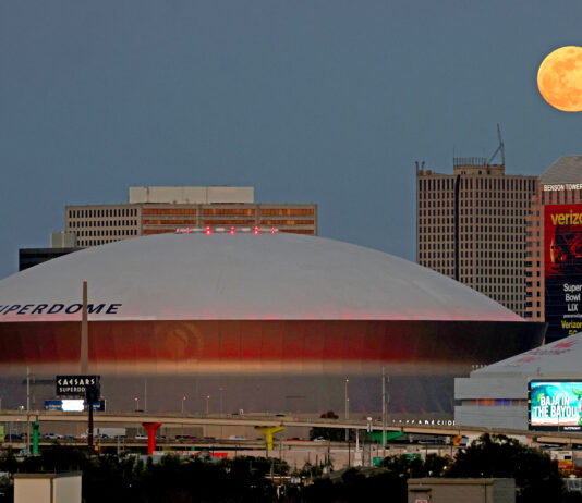 NASA Captures Stunning Moon Above Superdome The full moon (top right) rises over buildings in New Orleans, Louisiana, including the Superdome. The Superdome has a white rounded top. Billboards and ads can be seen around and on some of the buildings.