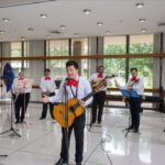 NASA Celebrates Hispanic Heritage: Introducing Manuel Retana A group of musicians, dressed in traditional mariachi attire with white shirts, red bow ties, and black pants, perform in a bright, spacious room. The lead musician stands at the front, holding a guitar and singing into a microphone.