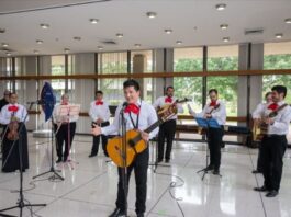 NASA Celebrates Hispanic Heritage: Introducing Manuel Retana A group of musicians, dressed in traditional mariachi attire with white shirts, red bow ties, and black pants, perform in a bright, spacious room. The lead musician stands at the front, holding a guitar and singing into a microphone.