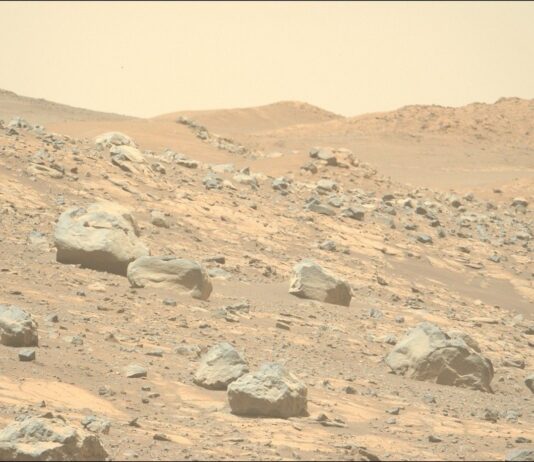 Perseverance Hunts for Signs of Contact Metamorphism on Mars A color photo from the surface of Mars shows very rocky terrain in the foreground sloping downward from left to right. The ground ranges in shades from orange-tan to brown, while the rocks are mostly gray. A trio of hills rises up in the distance.