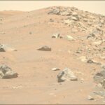 Connecting Regional Rock Formations to Broader Terrain: NASA Study A color photo from the Martian surface shows a landscape of sandy, rocky terrain. What looks like a pair of light orange-brown sand dunes rise in the background. Four or five large, sharp-edged rocks are strewn among the sand on the left side of the image. But a clear vertical dividing line extends from the center of the image to the right side, where the sand is covered by similar rocks of all sizes. A pale yellow sky is visible above the scene.