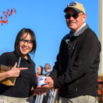 NASA and Notre Dame Unite to Encourage STEM Career Aspirations Portage School of Leaders High School junior Rebecca Anderson, wearing a black short-sleeved shirt and glasses, stands smiling beside NASA Glenn’s Daniel Sutliff, an acoustic engineer, on the campus of the University of Notre Dame. Sutliff is wearing a NASA ballcap and black jacket. He and Anderson are holding an autographed NASA mug, which Sutliff signed with a black ink permanent magic marker. Anderson is holding the black marker and a small cardboard box.