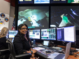 From Oceans to Space: Aaisha Ali’s NASA Journey A woman sits at a desk and poses in front of three monitors. Multiple monitors display live data and video of astronauts on the International Space Station. An American flag and NASA mission patches are visible on the wall behind her.